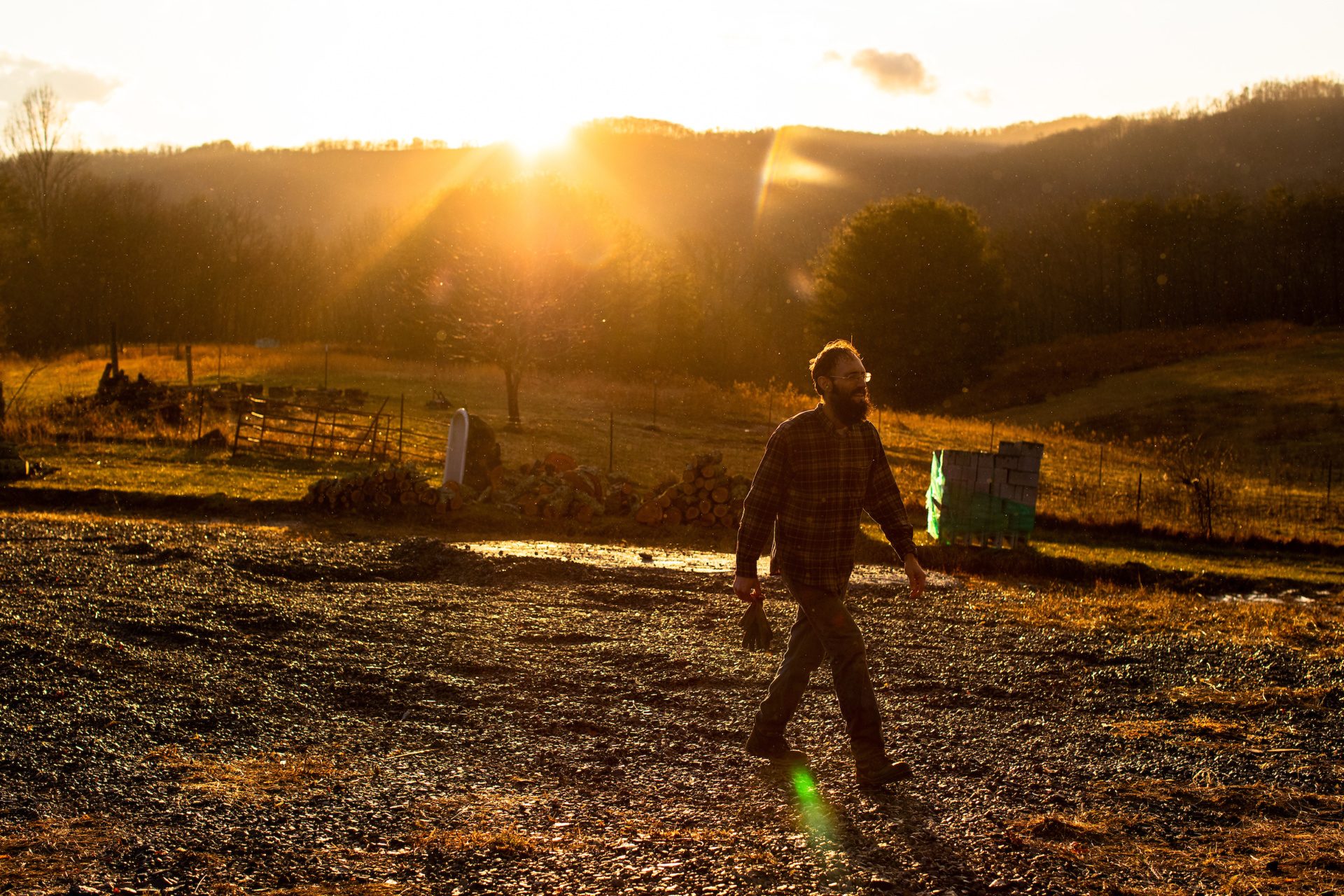 A Loyola University Chicago alumnus carries a pair of gloves as he walks over gravel on a farm at sunset