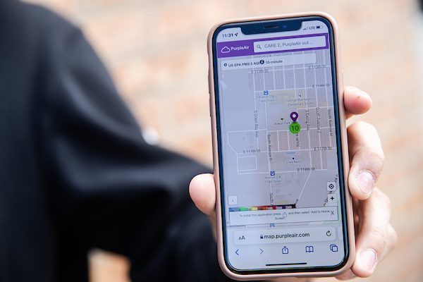 A close-up of a cellphone shows a map with the location of a recently installed air quality monitor