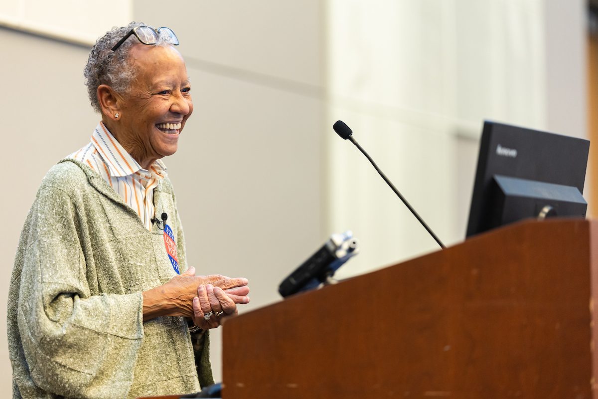 A Black woman smiles as she stands behind a podium