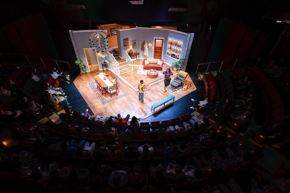 A lit-up stage of a living room surrounded by a darkened audience