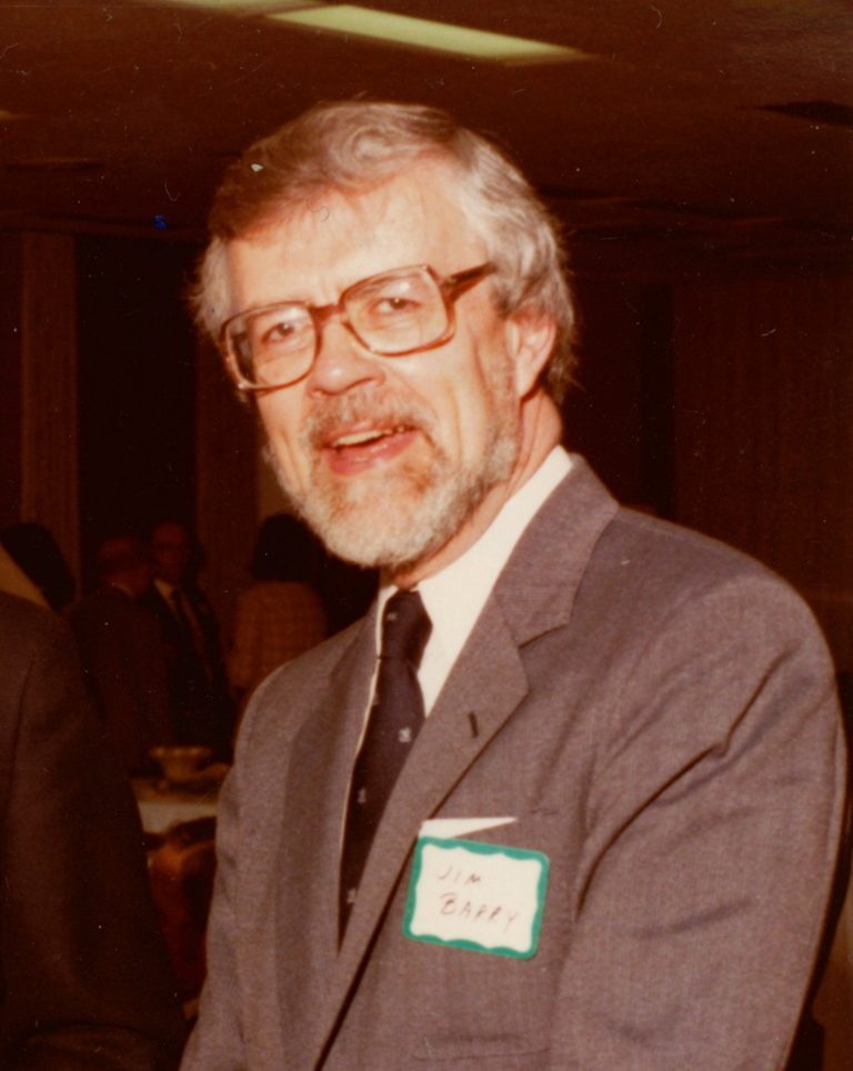 A man wearing glasses and a suit smiles in a sepia-toned photo